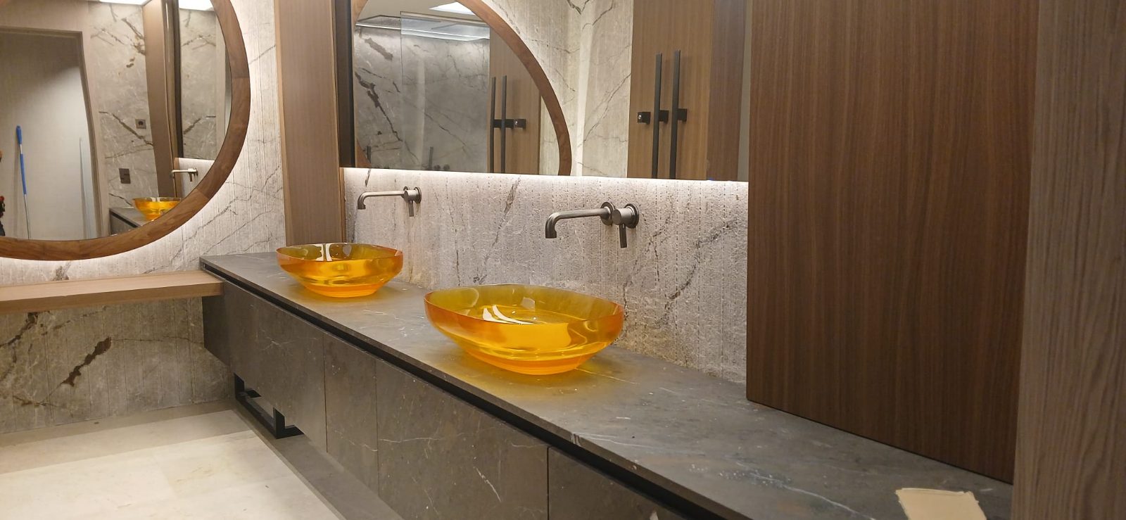 Baño de mármol con espejos redondos retroiluminados sobre la encimera