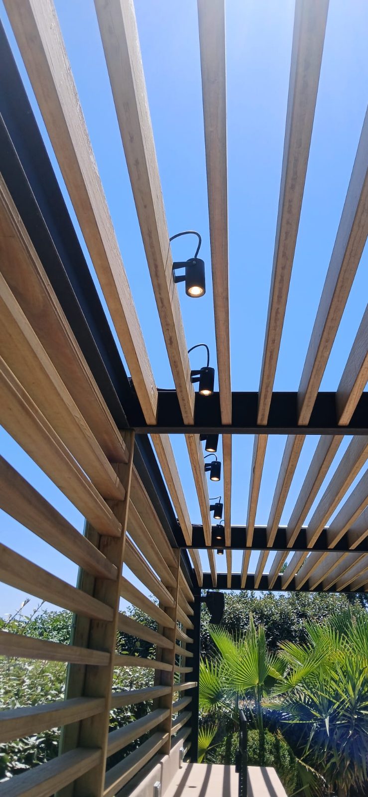 Pérgola de listones de madera con proyectores orientables montados en la estructura